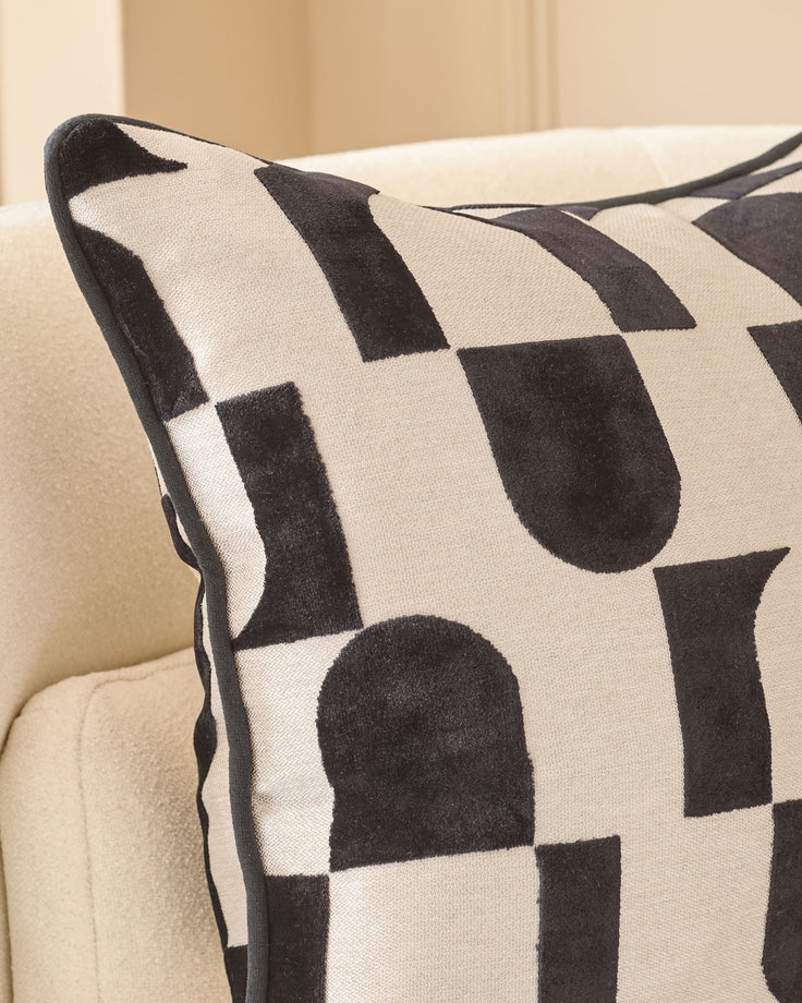 Black and cream geometric patterned cushion with piping detail, displayed on a neutral sofa.