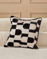 Black and cream geometric patterned cushion with piping detail, displayed on a beige sofa against a neutral wall.