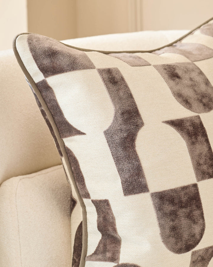 Bridget medium cushion in chocolate, featuring a geometric patterned design in brown and cream tones, placed on a neutral sofa.