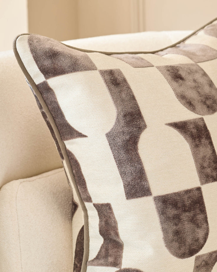 Bridget medium cushion in chocolate, featuring a geometric patterned design in brown and cream tones, placed on a neutral sofa.