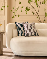 Bridget cushion in chocolate brown and cream geometric pattern, displayed on a cream curved sofa with decorative styling.