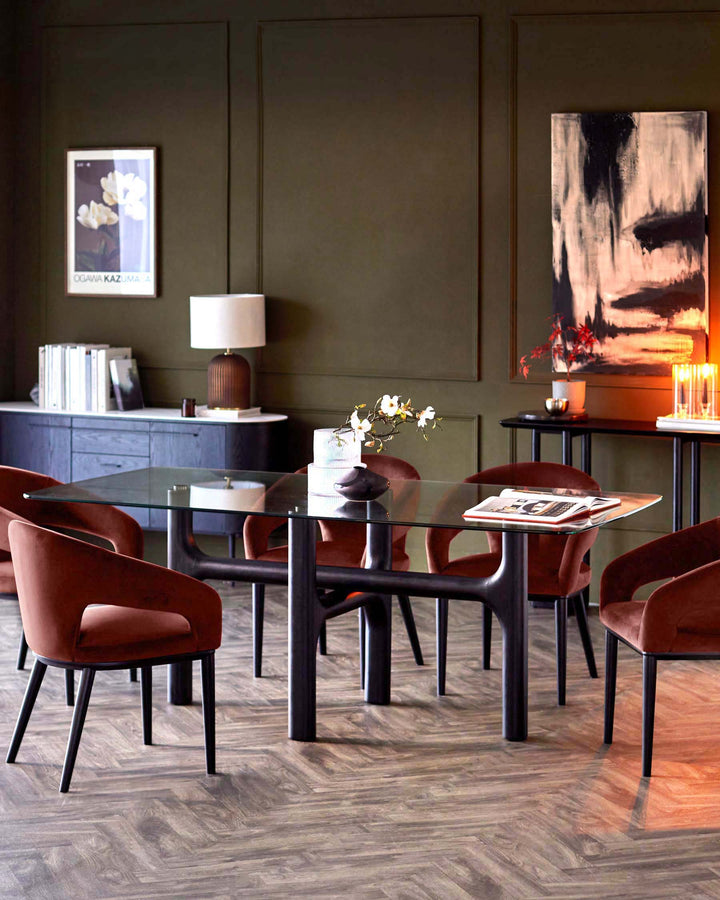 A contemporary dining room set with a glass-topped table and velvet chairs. Modern sideboard and console table in background.