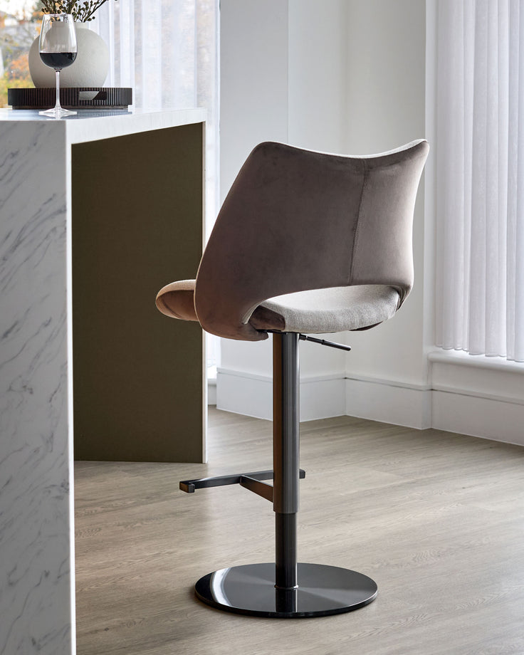 Bronwyn gas lift bar stool in mocha velvet and natural fabric with black metal base, shown in modern interior setting.