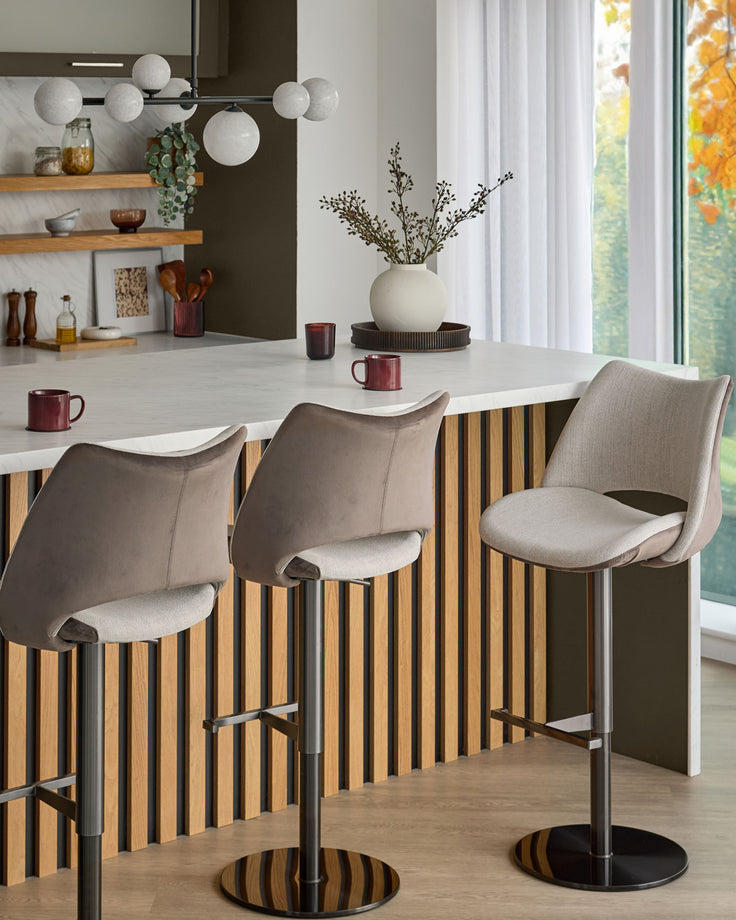 Bronwyn gas lift bar stool in mocha velvet with natural wood striped base and black pedestal, shown in kitchen setting.