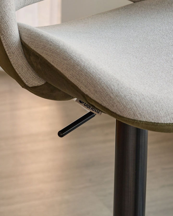 Bronwyn gas lift bar stool with natural fabric seat, olive green velvet back, and black metal base, detail view of handle.