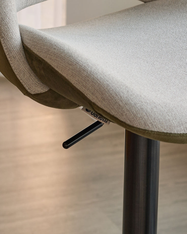 Bronwyn gas lift bar stool with natural fabric seat, olive green velvet back, and black metal base, detail view of handle.