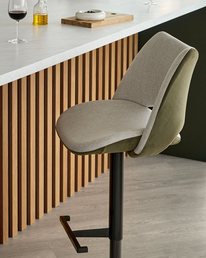 Bronwyn gas lift bar stool in natural and olive green velvet fabric, shown at a modern kitchen counter with vertical wood paneling.