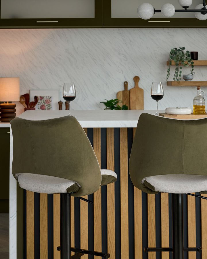 Bronwyn gas lift bar stools in olive green velvet and natural linen, shown at kitchen island with white countertop.