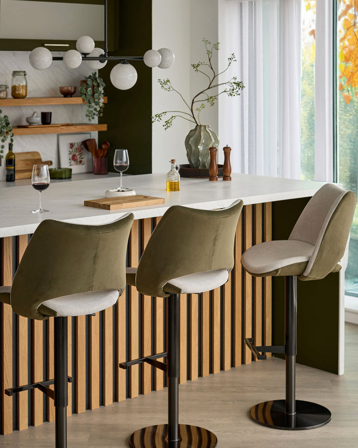 Bronwyn gas lift bar stools in olive green velvet with cream seat cushions, black metal base, shown at kitchen island.