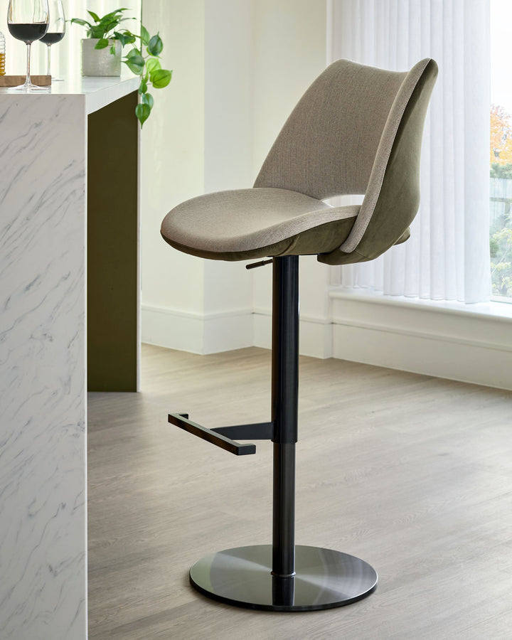 Bronwyn gas lift bar stool in natural and olive green fabric with black metal base and footrest, shown in kitchen setting.
