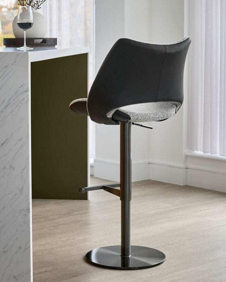 Bronwyn gas-lift bar stool with black faux leather back, grey fabric seat, and dark metal base in modern interior setting.