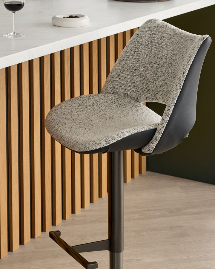 Bronwyn gas lift bar stool in grey fabric and black faux leather, shown at a kitchen counter with wooden slat detailing.