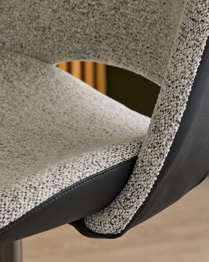 Close-up of Bronwyn bar stool showing grey fabric seat, black faux leather base, and curved armrest detail.