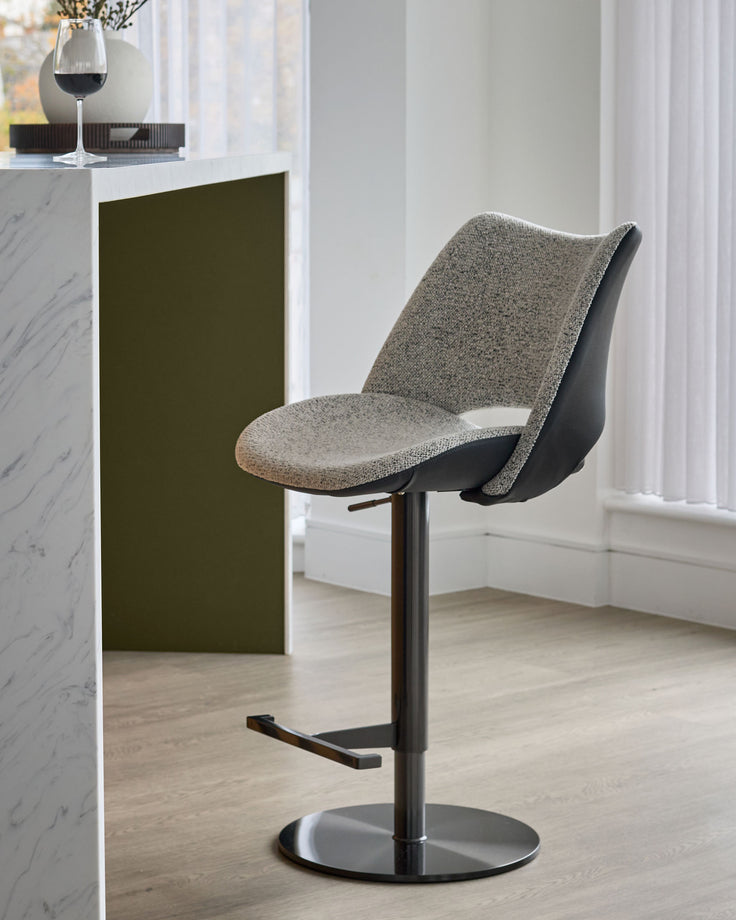 Bronwyn gas lift bar stool with grey fabric seat and black faux leather back, featuring a black metal pedestal base.
