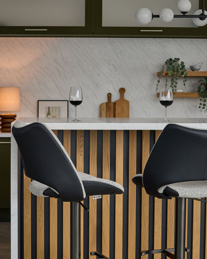 Bronwyn gas lift bar stool in grey fabric and black faux leather, shown at kitchen counter with wood and black metal frame.