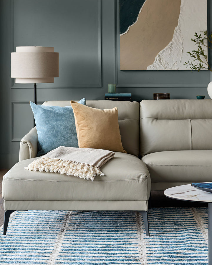Light grey leather left-hand corner chaise sofa with rolled arms, styled with blue and tan pillows and cream throw blanket.