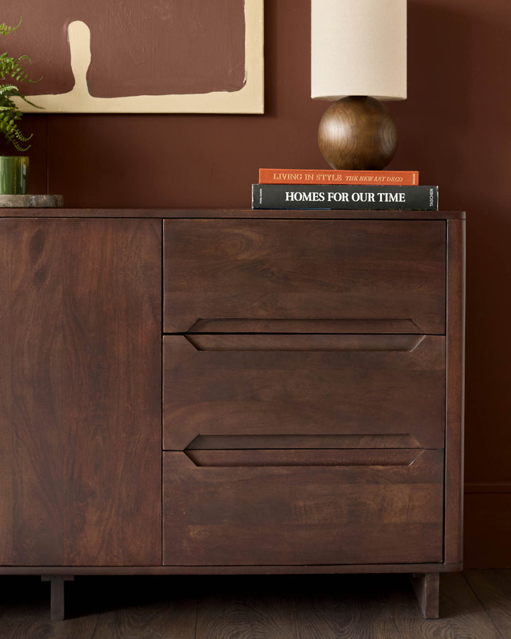 A dark wood sideboard with doors and drawers, topped with a lamp and books.