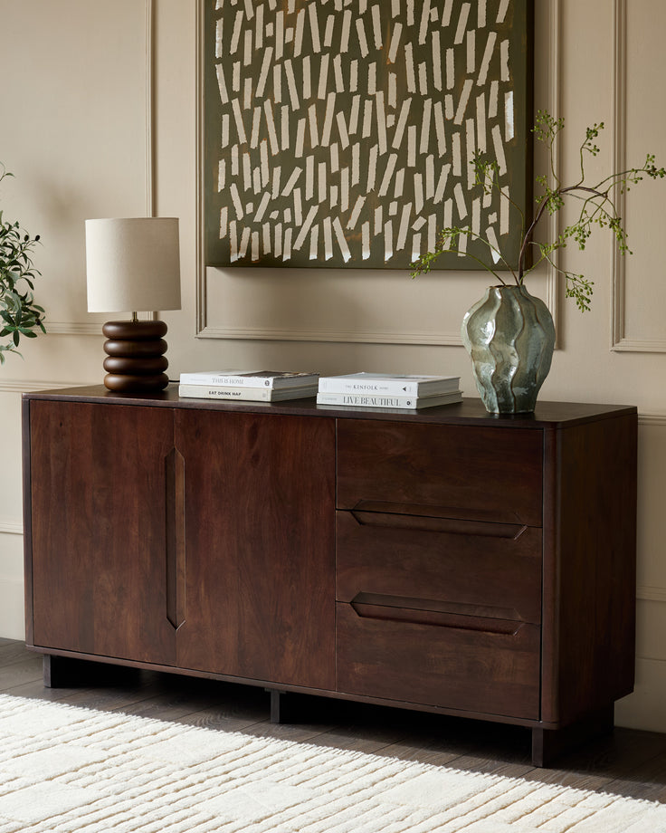 Dark mango wood sideboard with two cabinet doors and two drawers, displayed in a styled living room setting.
