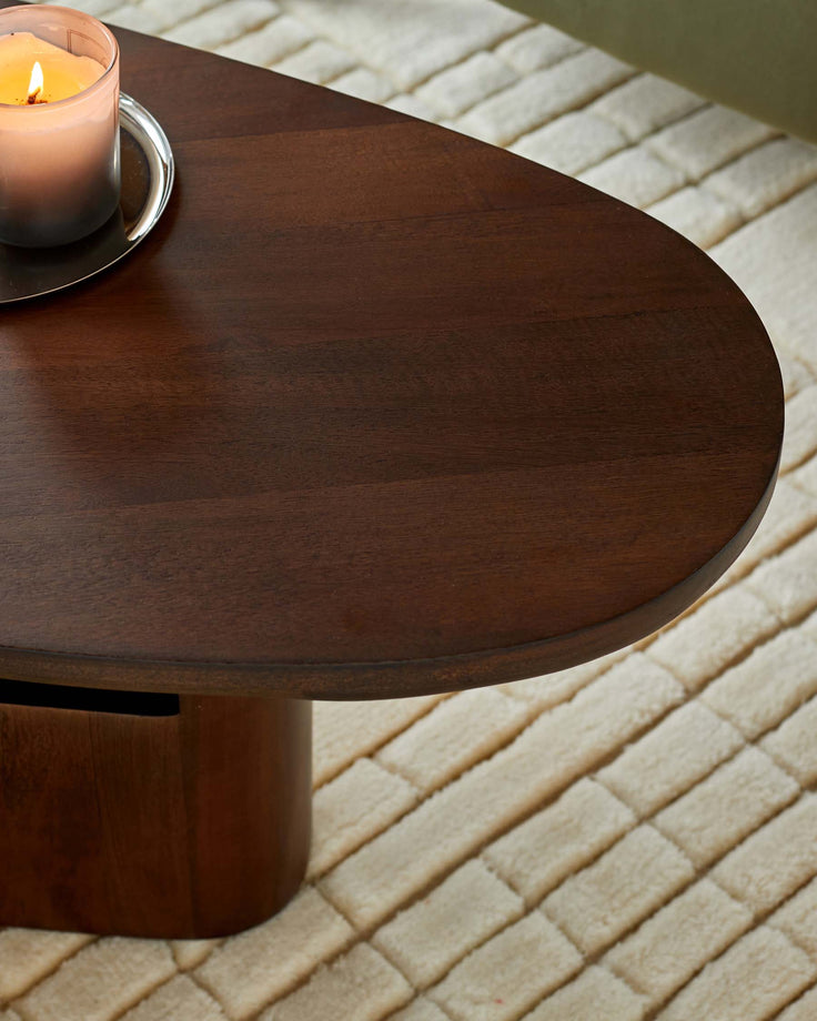 A sleek, dark-wood coffee table with a modern, oval design, complemented by a lit candle on a silver tray.