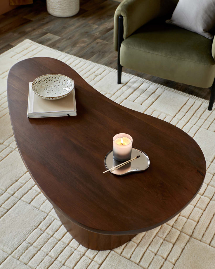 A stylish living room featuring a brown wooden coffee table, a decorative bowl, and a modern green armchair, all atop a cream rug.
