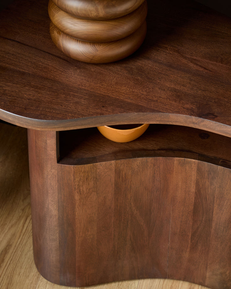 Dark mango wood side table with curved base and open shelf compartment, shown at angle.