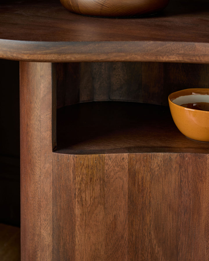 Dark mango wood side table with open shelf compartment and rounded wooden bowl on top surface, showing warm wood grain finish.