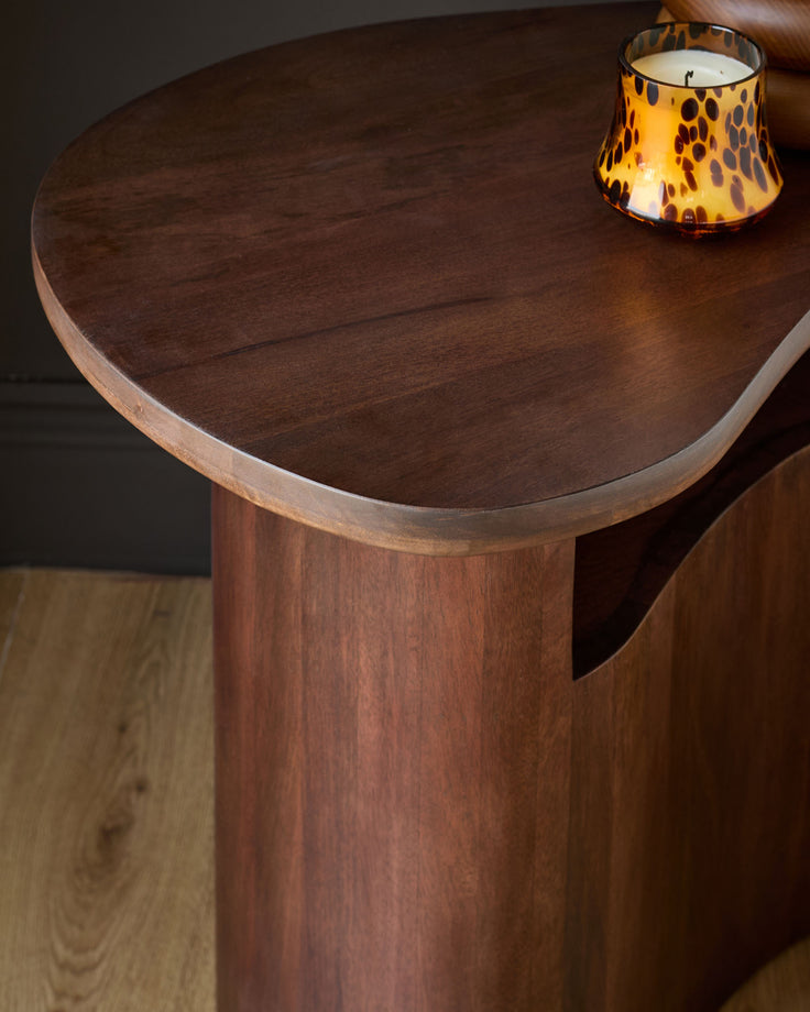 Dark mango wood side table with round top and cylindrical pedestal base, styled with a leopard-print candle.