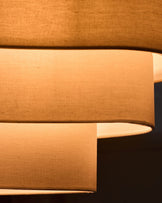 Natural linen pendant light with two cylindrical shades in warm beige, shown at an angle highlighting the fabric texture and form.