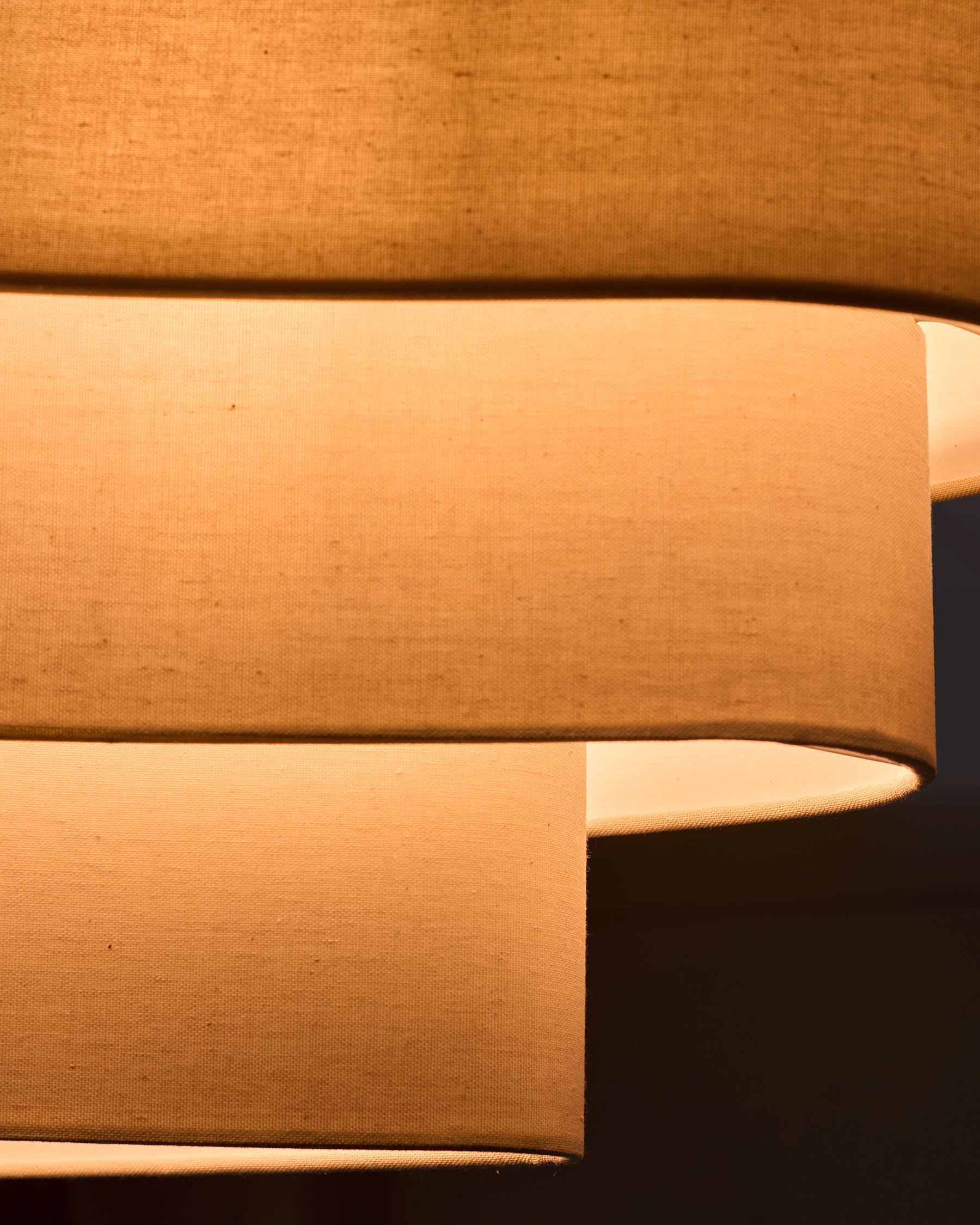 Natural linen pendant light with two cylindrical shades in warm beige, shown at an angle highlighting the fabric texture and form.