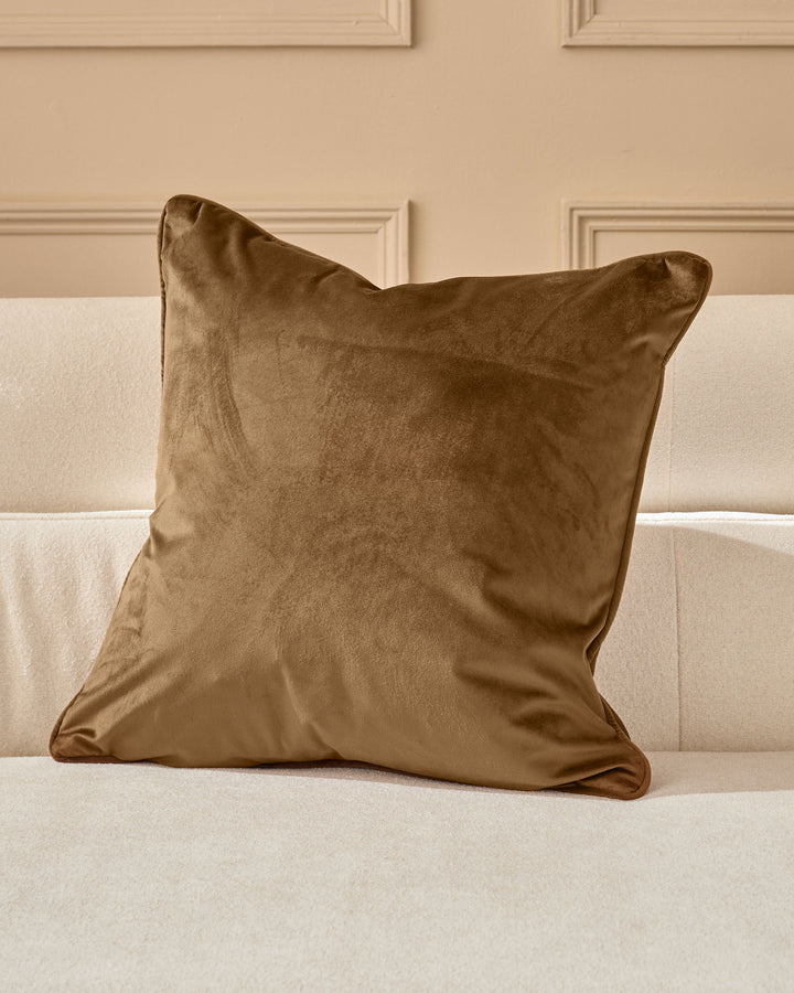Micah medium cushion in chocolate brown velvet displayed on a cream upholstered sofa against a beige paneled wall.