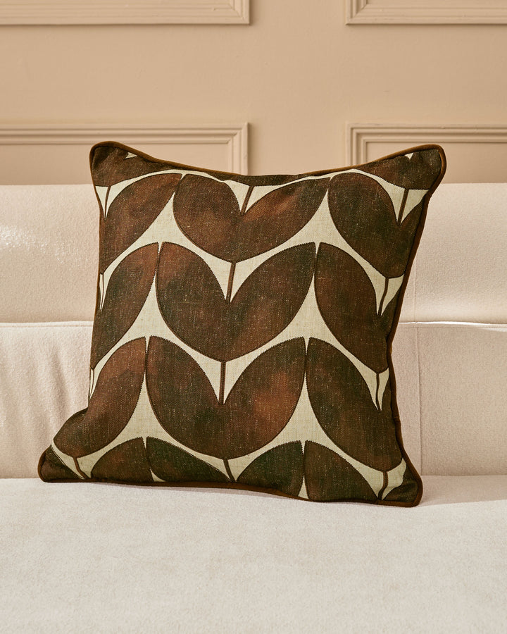 Micah cushion in chocolate brown with geometric leaf pattern on cream background, displayed on beige sofa.