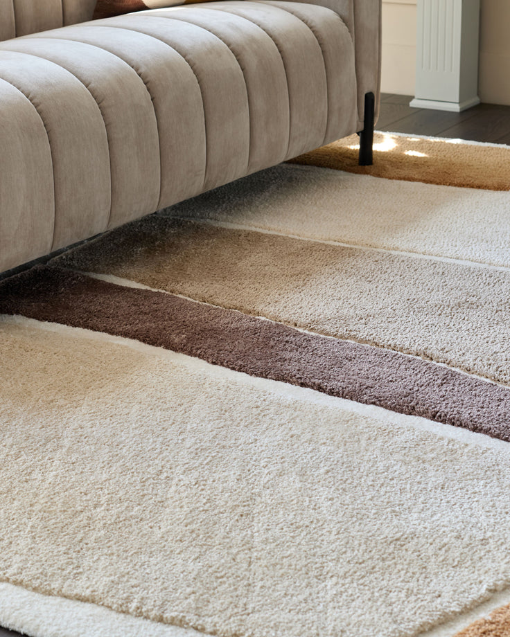 A beige, ridged sofa sits atop a patterned rug with cream, brown and tan stripes.