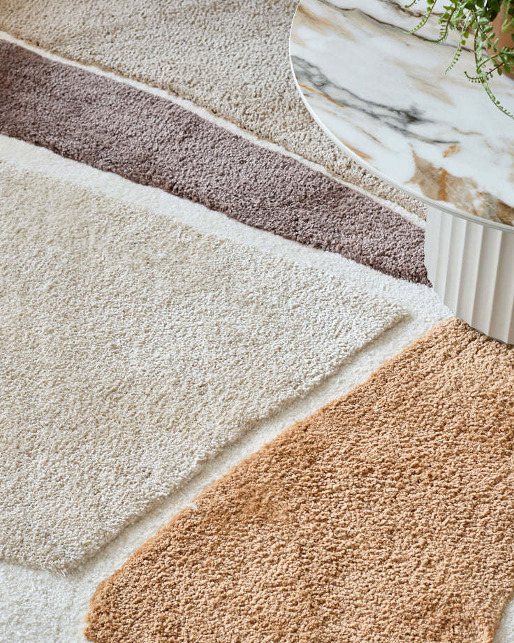Close up of a stylish rug with cream, brown and beige stripes next to a marble-effect table.