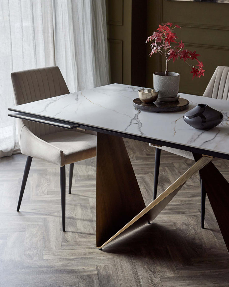 A stylish marble dining table with unique triangular wooden legs, paired with a plush, upholstered chair in soft tones.