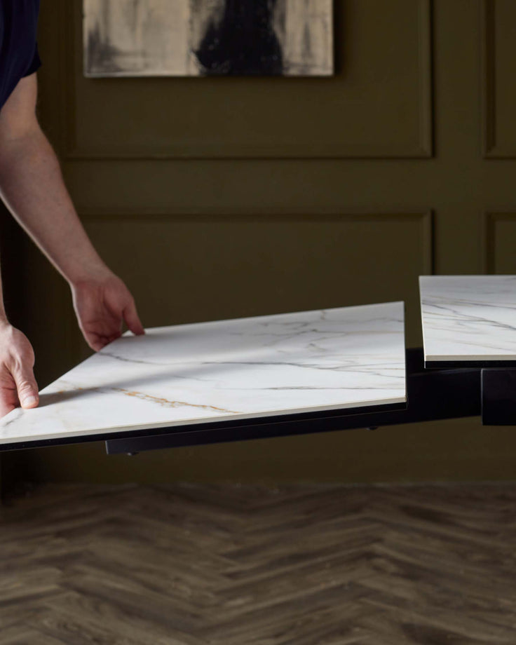A sleek, modern table featuring white marble surfaces with subtle gold veining, being adjusted for size.