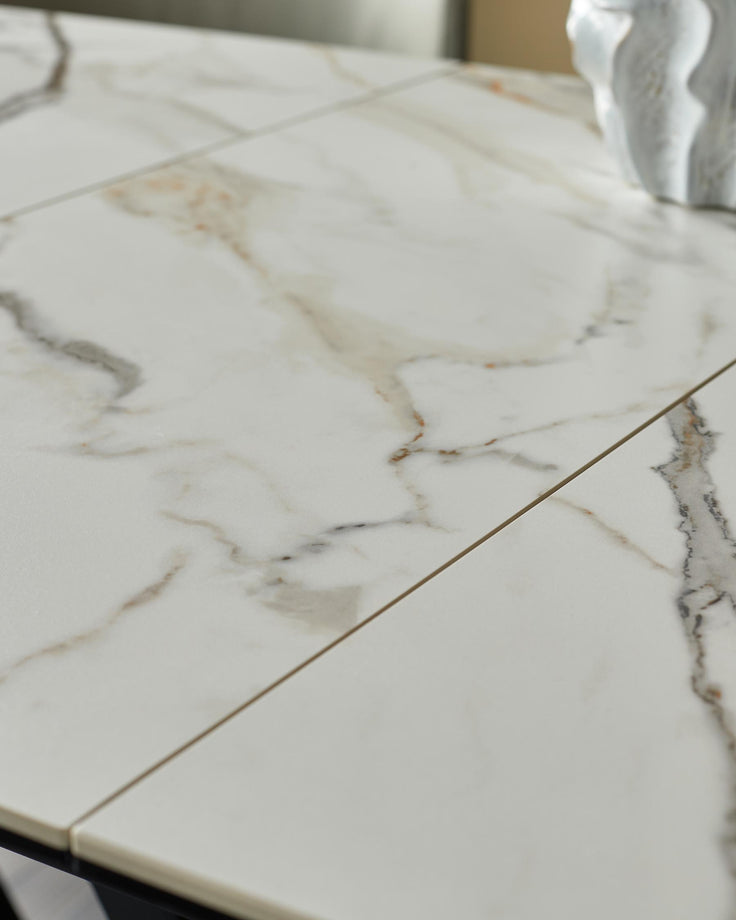 Close-up of a white marble-effect extendable dining table with a modern decorative piece. Elegant and contemporary design.
