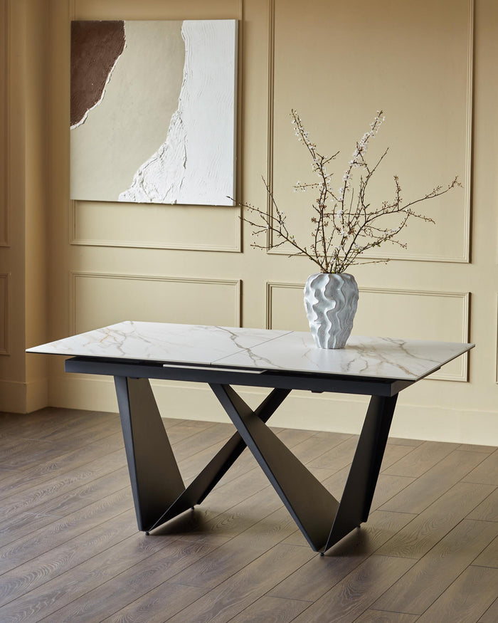 A modern marble-effect table with a unique black angular base, topped with a sculptural vase and branches.