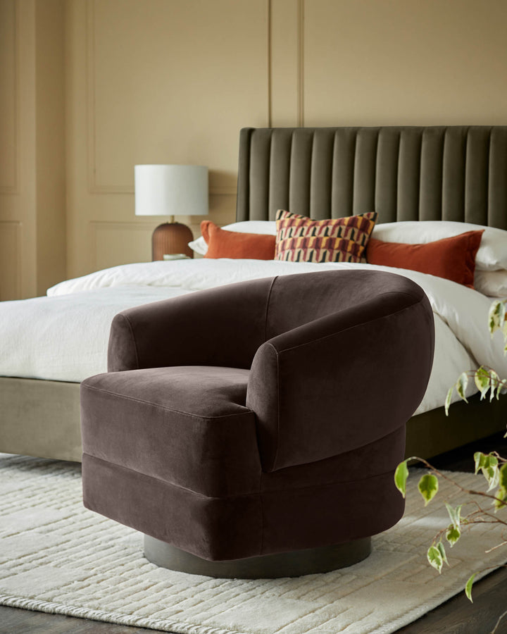 A brown velvet swivel armchair sits in front of a bed with a green headboard and white duvet, on a cream rug.