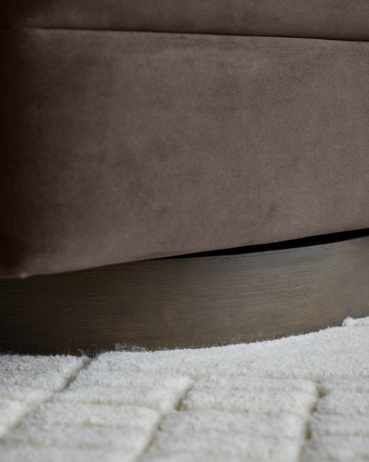 Close-up of a brown swivel chair with a wooden base on a white shag rug.
