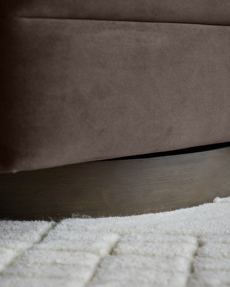 Close-up of a brown swivel chair with a wooden base on a white shag rug.