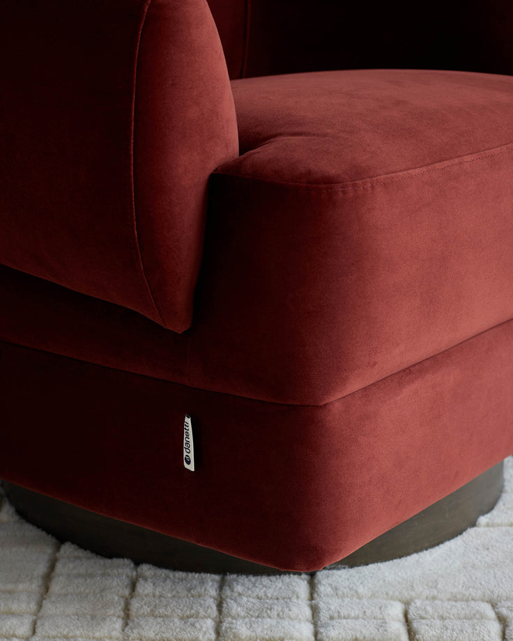 Close-up of a red velvet armchair with a round, dark wood base on a white rug.