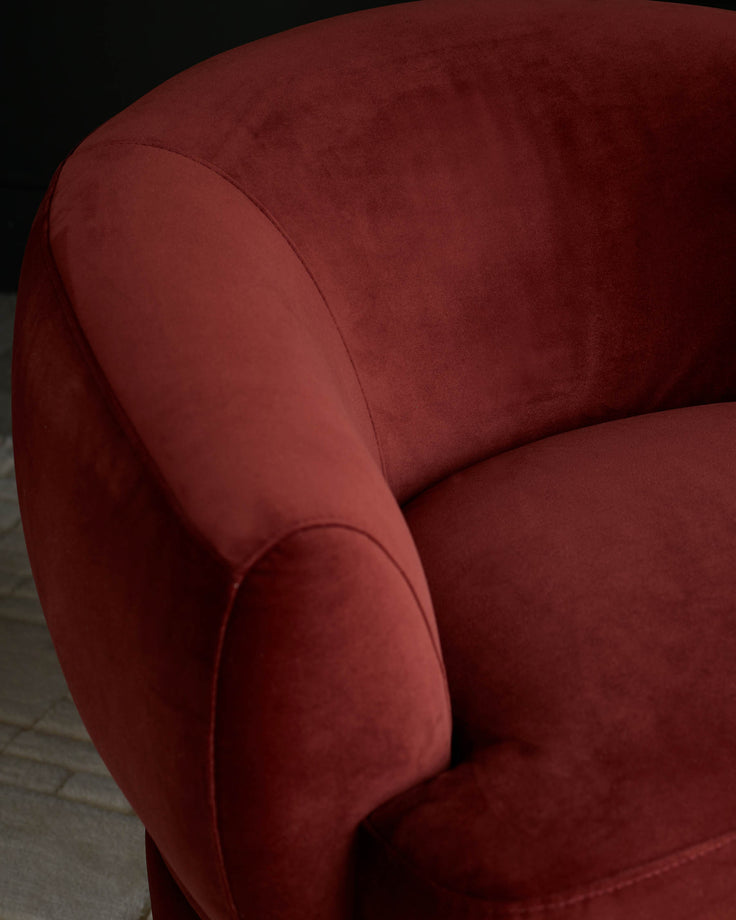 Close-up of a plush, red velvet armchair, showcasing its curved arm and seat. Ideal for a cosy living space.