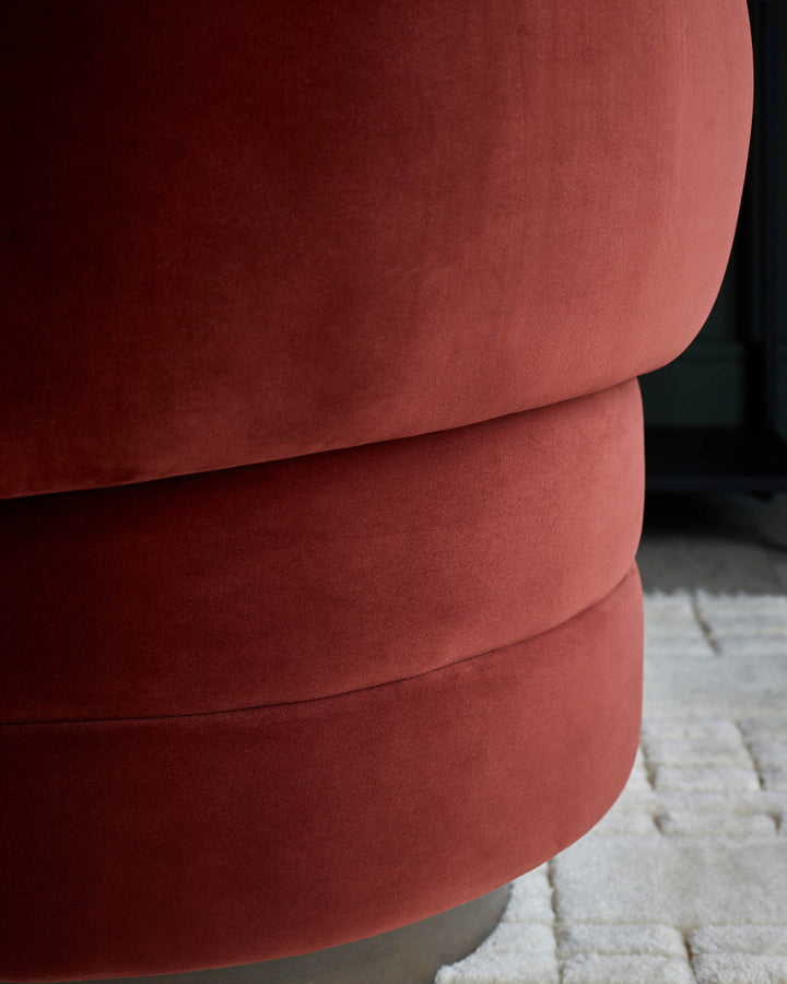 Close-up of a plush, red velvet ottoman with a tiered design, resting on a stylish, patterned rug.