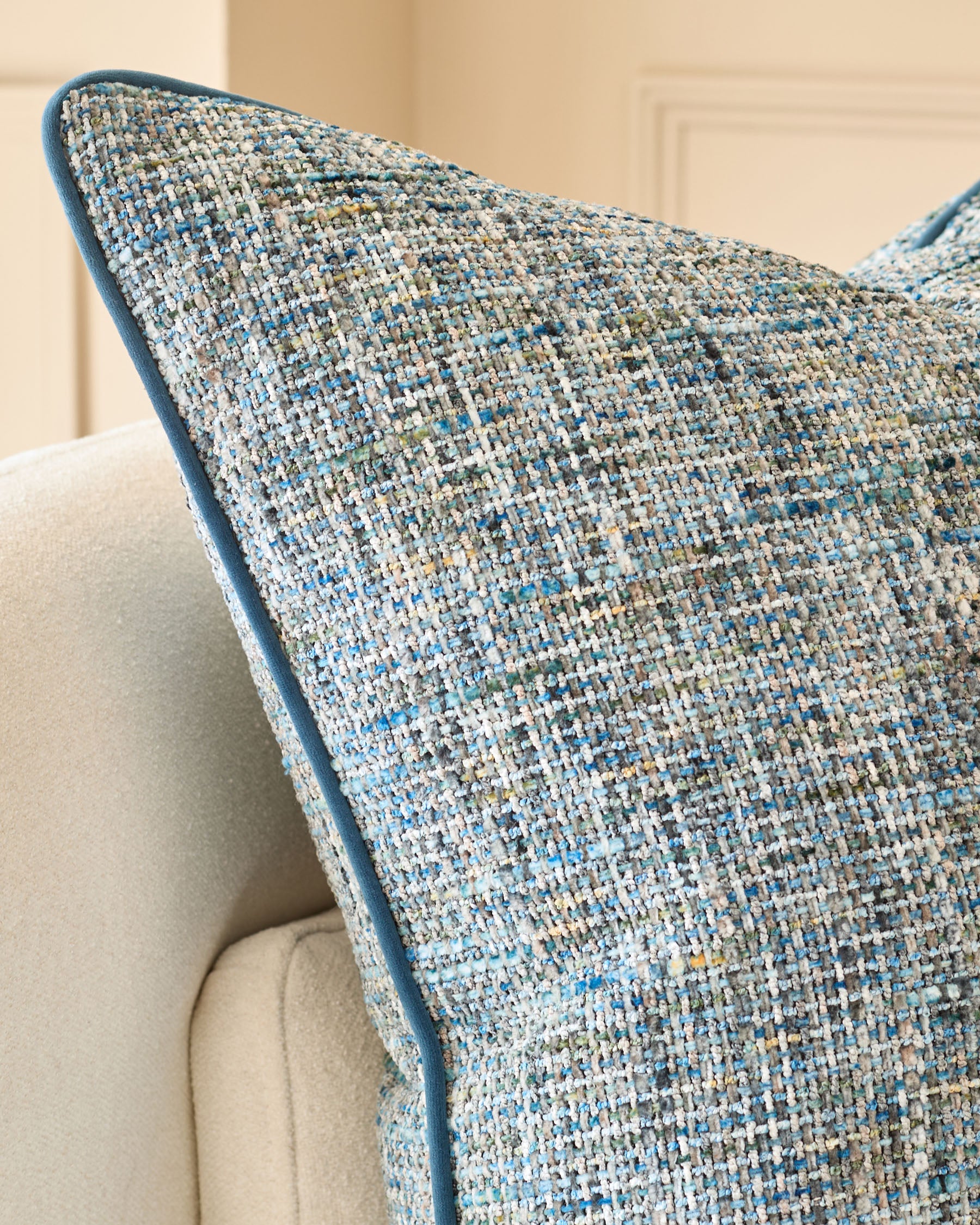 Large blue textured cushion with woven fabric detail, displayed on a cream upholstered chair arm.