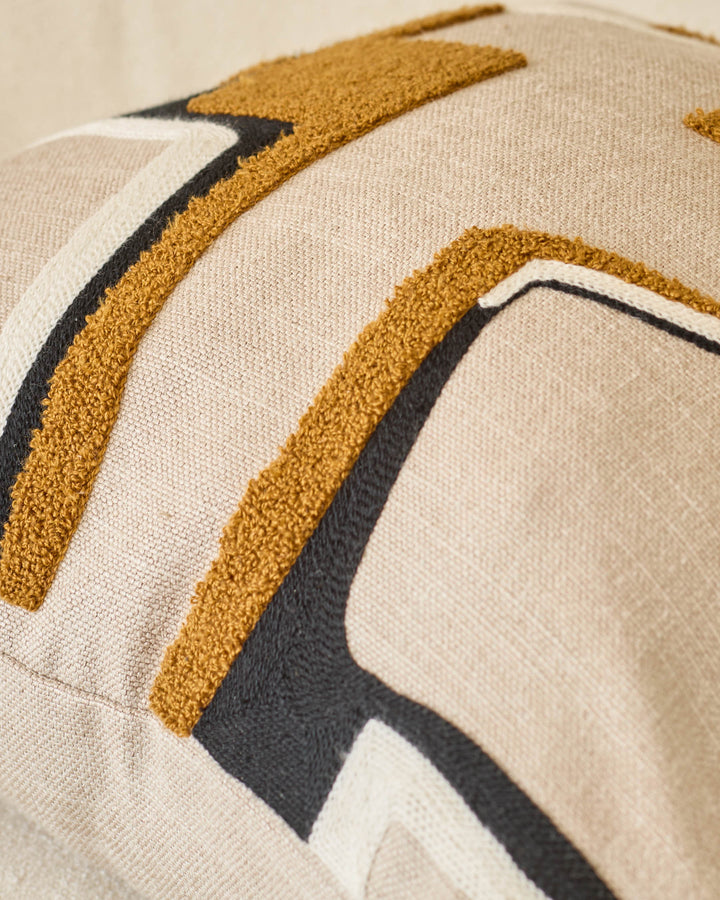 Camille cushion in natural with gold, black and cream geometric embroidered design, close-up detail view.