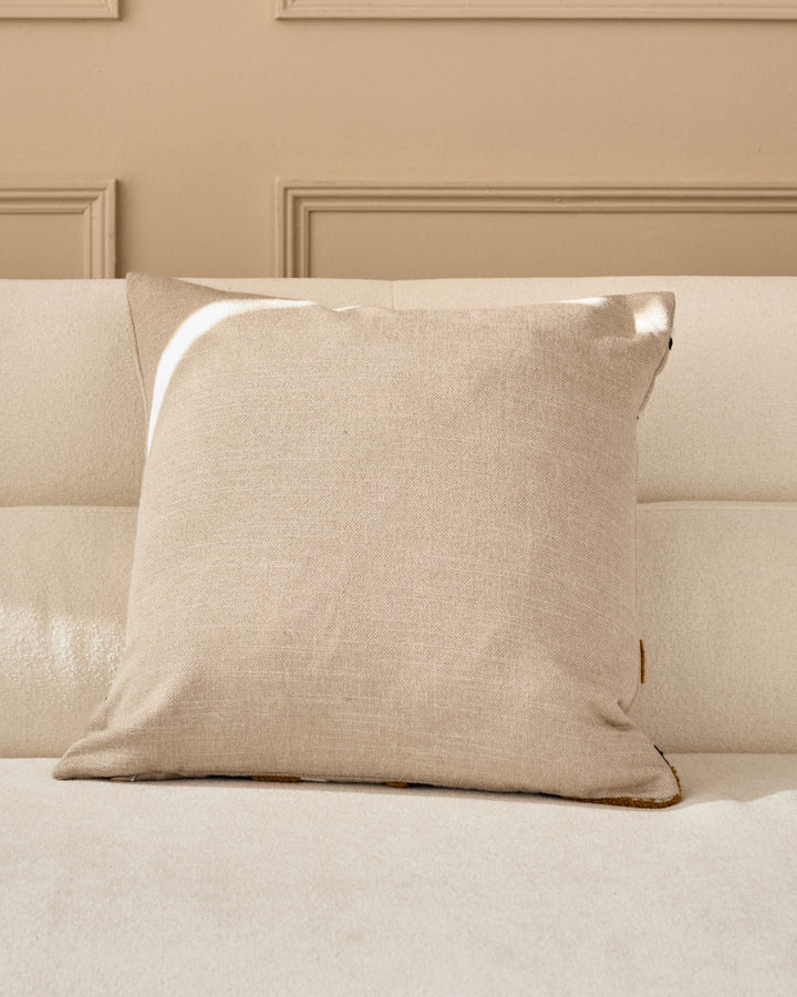 Camille cushion in natural linen on a neutral upholstered sofa, featuring a square shape with visible stitching details.