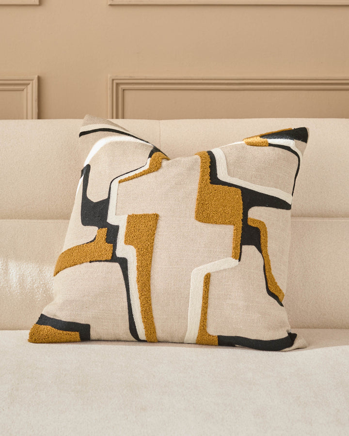 Camille medium cushion in natural with geometric gold, black and cream pattern, displayed on a beige sofa.