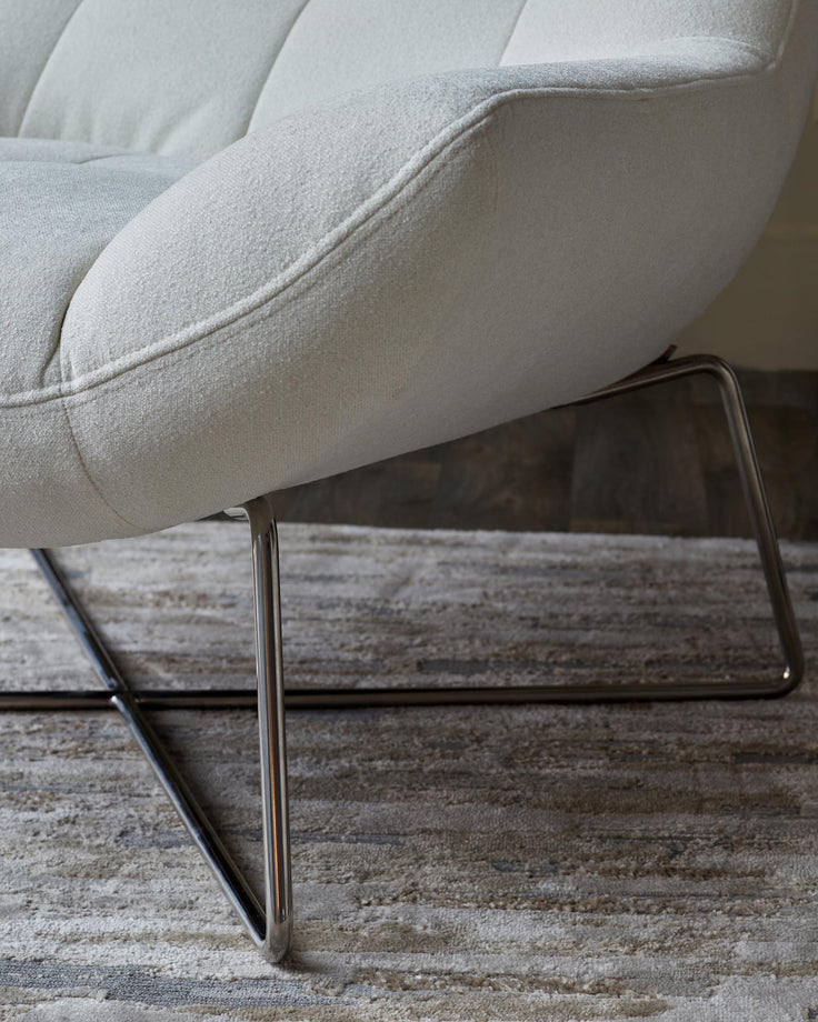 Close-up of a stylish, modern chair with chrome legs and light-coloured upholstery, showcased on a patterned rug.