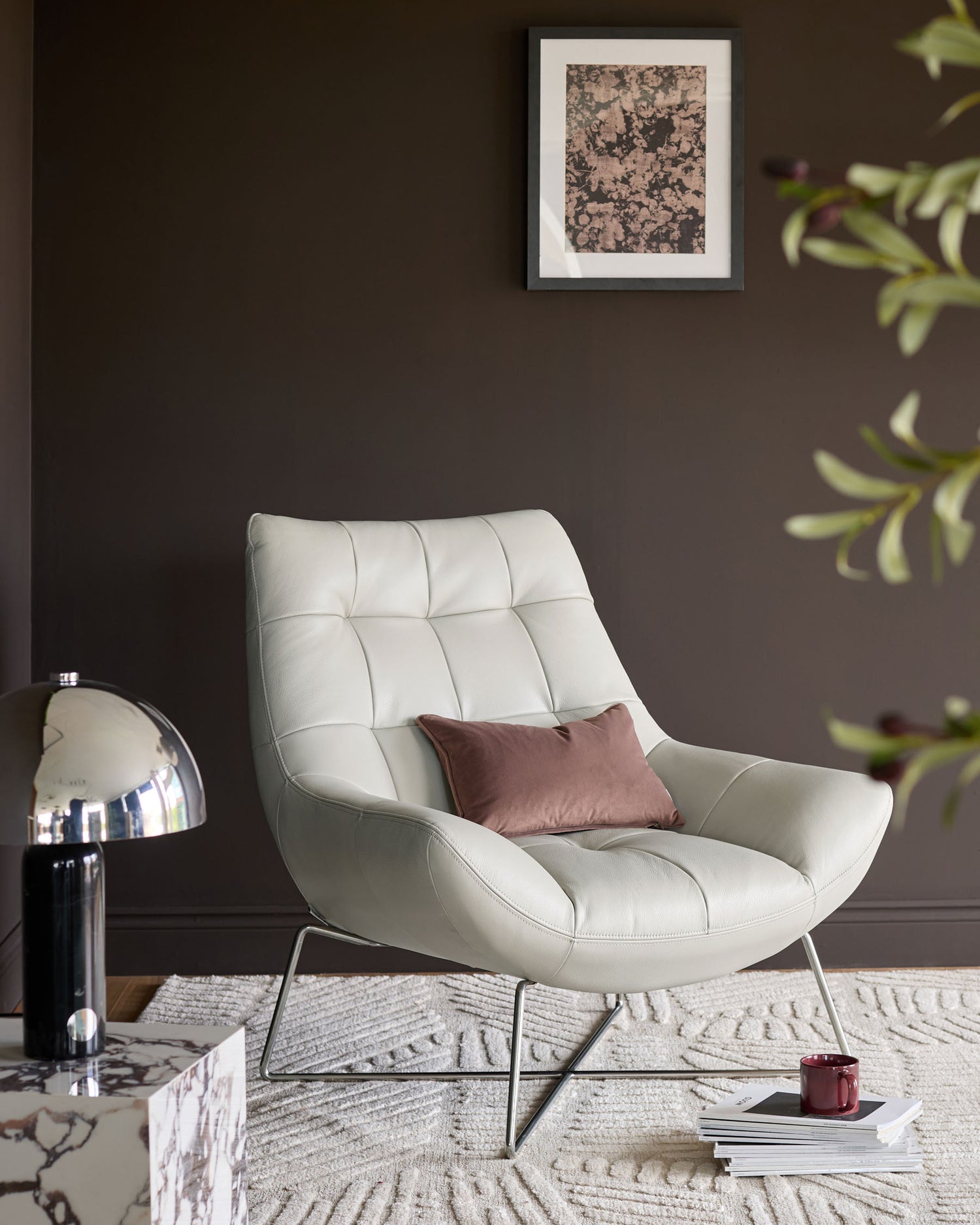 Canio leather armchair in natural grey with brushed steel frame, shown in a styled living room setting with cushion.