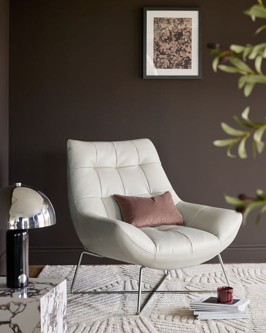 Canio leather armchair in natural grey with brushed steel frame, shown in a styled living room setting with cushion.